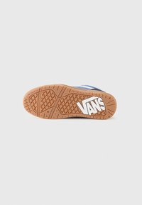 Vans sneaker sole, featuring a tan rubber base with a textured grip pattern, "VANS" logo in white, and blue accents near the sides.