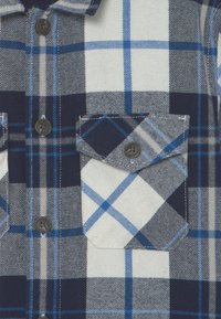 Kostkovaná košile v námořnické, bílé a světle modré barvě. Bavlněný materiál s knoflíkovým zapínáním a dvěma náprsními kapsami.