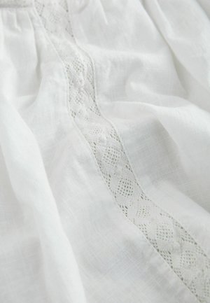 White fabric with a delicate vertical lace panel featuring floral and geometric patterns, softly wrinkled and textured.