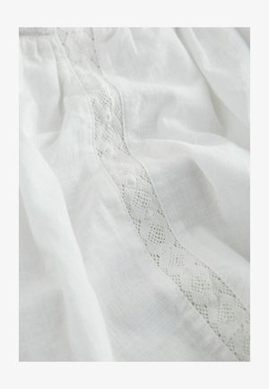 White fabric with a delicate vertical lace panel featuring floral and geometric patterns, softly wrinkled and textured.