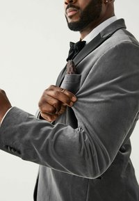 Grau samtenes Blazer mit klassischem Revers, einer Brusttasche, die ein gemustertes Taschentuch zeigt, und taillierten Manschetten, die eine glatte Oberfläche präsentieren.