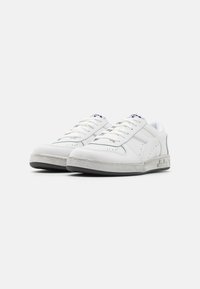 White leather sneakers with grey rubber soles, featuring perforated detailing, flat laces, and a side logo accent. Smooth texture overall.