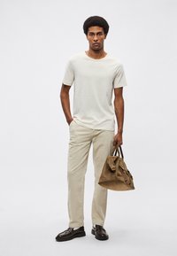 Μπεζ πουκάμισο με κοντά μανίκια, ανοιχτόχρωμο παντελόνι, καφέ δερμάτινα παπούτσια, κρατώντας καφέ τσάντα ώμου. Λείες υφές, άνετη εφαρμογή, μινιμαλιστικός σχεδιασμός.