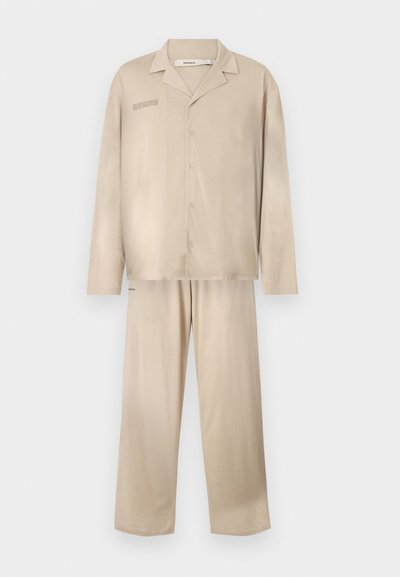 Beige lõõgastav komplekt, mis on valmistatud pehmest kangast, sisaldab pikkade varrukatega nööpidega särki ja sobivaid laia lõikega pükse.