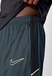 Szare sportowe szorty z lekkiego materiału, z czarnym panelem bocznym, elastycznym paskiem w talii oraz żółtym logo Nike z przodu.