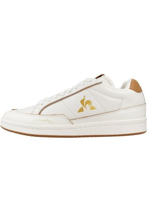 Zapatilla de cuero blanca con logo dorado, detalles en marrón claro en el talón y suela de goma texturizada. Estilo de cordones con acabado suave.