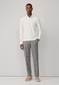 Polo shirt bianco a maniche lunghe con colletto, abbinato a pantaloni beige su misura e scarpe slip-on beige. Tessuto morbido e vestibilità classica.