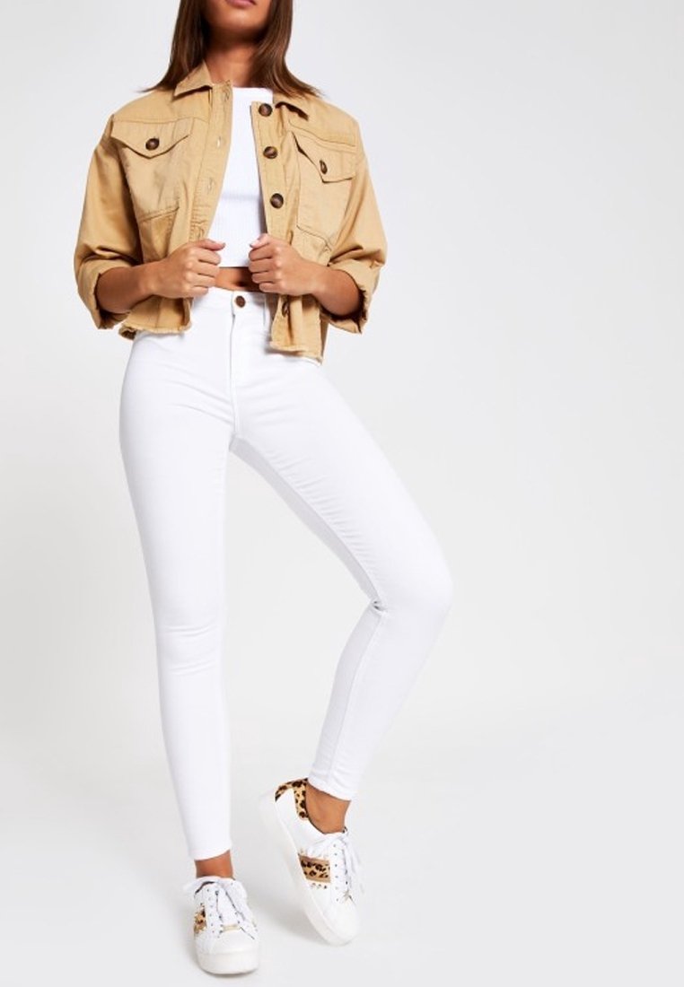 Kerman takki, jossa on kaksi rintataskua, valkoinen lyhyt toppi, korkeavyötäröiset valkoiset farkut ja valkoiset lenkkarit eläinkuosilla.