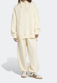 Sudadera de gran tamaño en color crema con un bolsillo canguro delantero y un logo sutilmente grabado, combinada con pantalones anchos de crema y zapatillas de color claro.