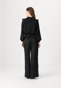 Blusa nera con dettagli arricciati e vita elastica, abbinata a pantaloni neri con gamba larga. Tessuto liscia, design elegante, dettagli minimi.