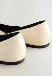 Weiße Kunstleder-Ballerinas mit einem geprägten Krokodil-Muster und einer schwarzen strukturierten Sohle. Runde Absätze und keine sichtbaren Hardware-Details.
