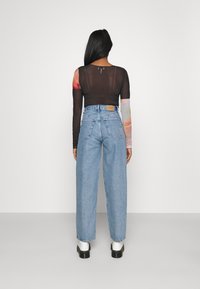 Svart mesh långärmad topp med färgglada mönstrade ärmar, kombinerad med högmidjade ljusblå denimjeans och vita platåskor.