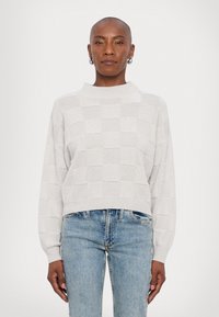 Maglione grigio chiaro a girocollo con motivo a scacchi, caratterizzato da un collo alto e maniche ampie, abbinato a jeans blu.