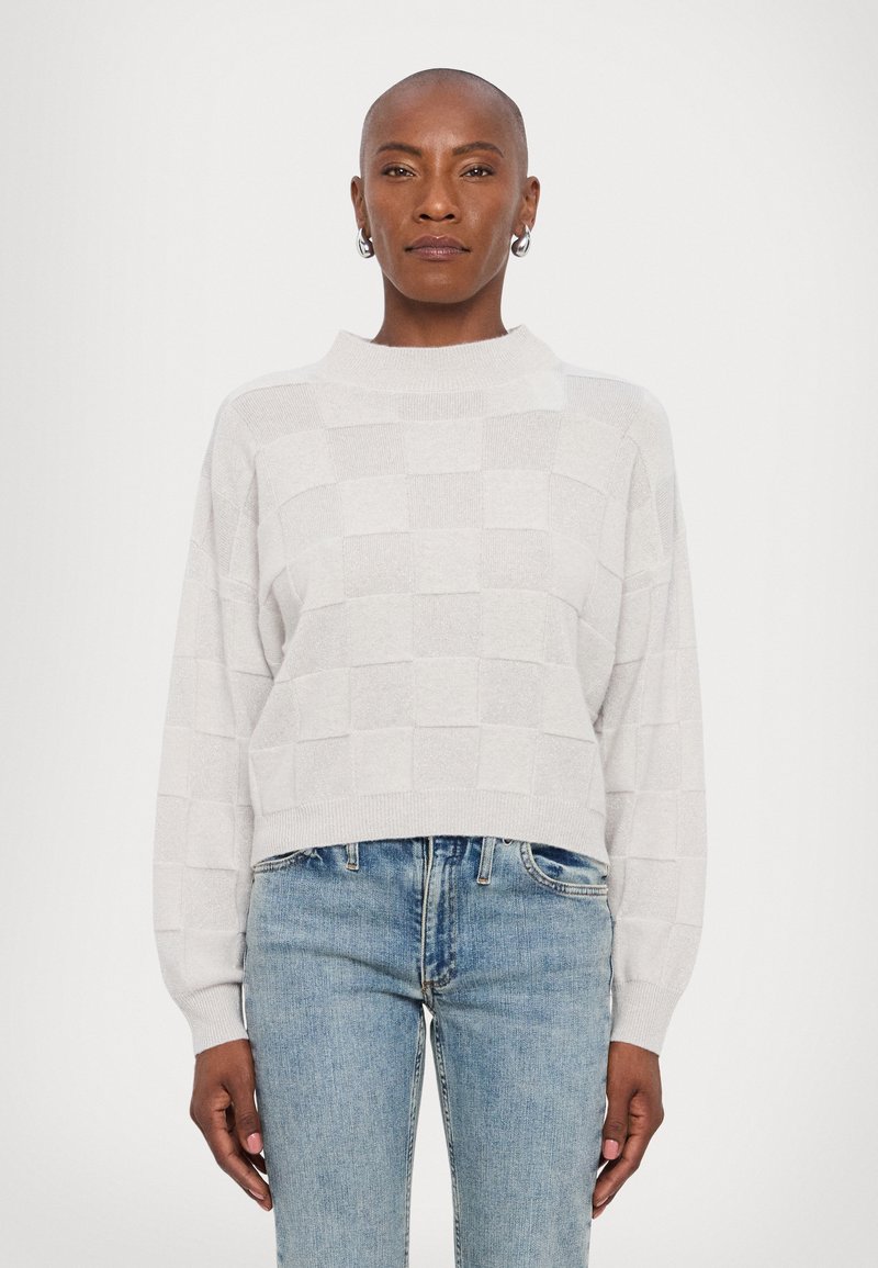 Maglione grigio chiaro a girocollo con motivo a scacchi, caratterizzato da un collo alto e maniche ampie, abbinato a jeans blu.