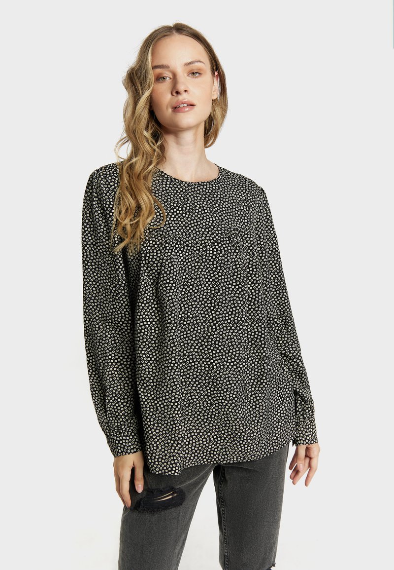 Blouse noire avec un col rond, des manches longues et un motif de petits points blancs. Fabriquée en tissu léger avec une coupe décontractée.