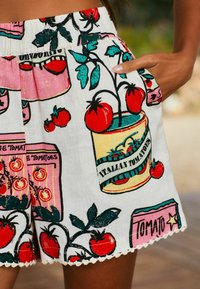 Short blanc avec un motif à thème de tomates, comprenant des tomates rouges, des feuilles vertes et des motifs décoratifs d'emballage. Taille élastique et bordure en dentelle.