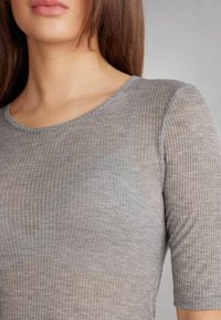 Top en tissu côtelé gris avec un col rond et des manches courtes. Le matériau a une texture légèrement transparente, mettant en avant des lignes subtiles.