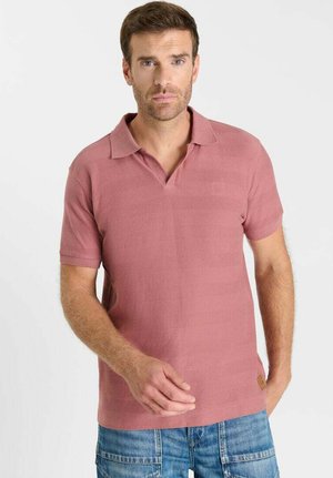 Lichtroze poloshirt van gestructureerde stof met een klassieke kraag, korte mouwen en een klein logodetail. Gecombineerd met een blauwe spijkerbroek.