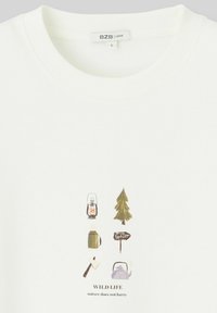 T-shirt blanche avec un imprimé graphique d'éléments de camping : une lanterne, un arbre, une bouteille d'eau, un panneau, une hache et le texte « VIE SAUVAGE ». 