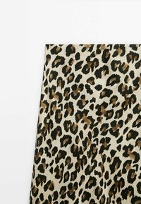 Tissu imprimé léopard avec des taches noires et marron sur fond beige, présenté à plat sur une surface blanche.