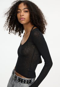 Top nero a maniche lunghe con scollatura a V profonda e tessuto leggero e trasparente. Presenta maniche aderenti e orlo corto.