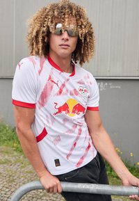 Baltas sportinis marškinėlis su raudonomis detalėmis, su grafiniu dizainu, Red Bull logo ir mažu Puma logotipu. Lygi medžiaga su pritaikytu siluetu.