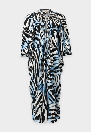 Femme portant une robe midi à imprimé zèbre abstrait noir, blanc et bleu, manches longues, et des sandales à talons noirs.