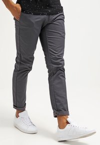 Pantaloni grigi affusolati con una texture liscia, caratterizzati da orli arrotolati e tasche laterali, abbinati a sneakers bianche. Design semplice e moderno.