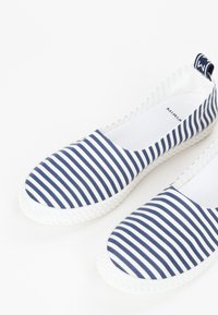 Scarpe slip-on in tela a righe blu e bianche con suola in gomma bianca testurizzata e linguetta in tessuto sul tallone.