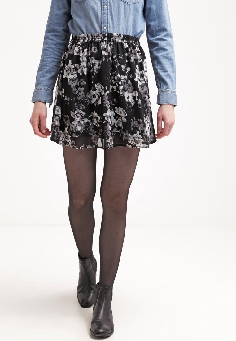 Jupe florale noire en tissu transparent avec une taille élastique, associée à des collants noirs et des bottines, portée avec un haut ajusté.