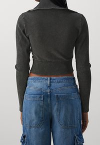 Afskåret sort ribbet langærmet top med høj krave, parret med blå denim cargo bukser med store lommer og knaplukning.