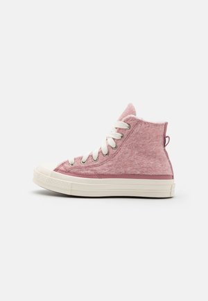 Baskets montantes avec tissu duveteux rose, lacets blancs et semelle en caoutchouc blanche sur fond blanc uni.