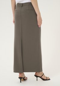 Pantalon large, vert olive foncé avec une texture lisse, doté de deux poches arrière et d'une taille mi-haute. Associé à des sandales à talons noires.