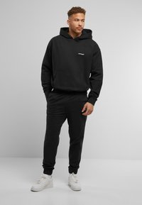 Black sweatshirt with hood and front pocket, paired with matching joggers. Soft texture, relaxed fit, featuring a small logo on the chest.