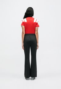Top rojo de manga corta con detalles en blanco y pantalón de pierna ancha con cintura elástica negra. Textura suave, diseño atlético y estilo minimalista.