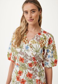 Vit omlottklänning med blommönster i röd, gul, blå och grön. Har korta puffärmar och ett knytliv för justerbar passform.