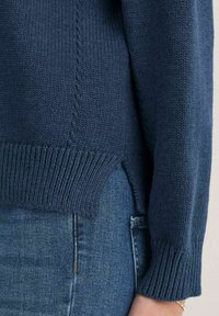 Merensininen neulottu villapaita, jossa on resorireunukset hihansuissa ja helmassa. Alareunassa sivuhalkiot rentoa istuvuutta varten. Pehmeä pinta, keskivahvuinen.