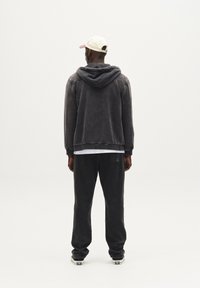 Dark gray hooded sweatshirt with a relaxed fit, paired with matching sweatpants. Features soft material and ribbed cuffs. White cap with pink brim.