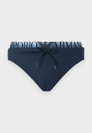 Marineblaue Herren-Badehose mit Kordelzug vorne und elastischem Bund mit "EMPORIO ARMANI" Schriftzug und Logo in Marineblau auf hellblauem Hintergrund.