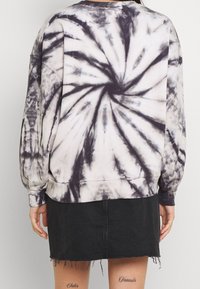 Sudadera de tie-dye en negro y crema, con un patrón en espiral. El diseño tiene un corte relajado y puños acanalados, combinado con una falda de mezclilla negra.