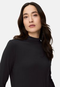 Czarny golf z długimi rękawami, wykonany z gładkiej tkaniny, o dopasowanym kroju podkreślającym sylwetkę.