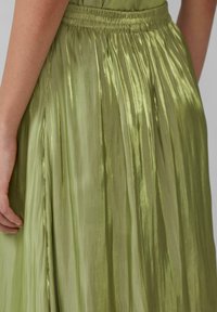 Jupe plissée verte avec une texture brillante et satinée, dotée d'une taille élastique. Le tissu tombe délicatement, mettant en valeur son design fluide.