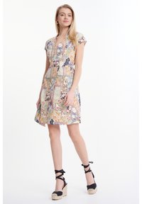 Kanten jurk met bloemenpatroon in pastelkleuren, met een v-hals en korte mouwen. Gepaard met zwarte espadrille sleehakken met enkelbandjes.