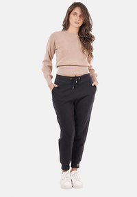 Pantaloni jogger neri con tasche, vita elastica, cordino regolabile e polsini a costine, abbinati a un maglione fitted beige e sneakers bianche.