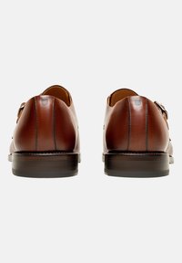 Braune Leder-Schuhe mit abgerundetem Absatz, glatter Textur und kontrastierenden Nähten. Sie verfügen über einen doppelten Riemenverschluss für sicheren Halt.