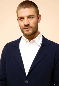 Marinblå wool cardigan med sjalkrage, stängning med en knapp, bärs över en vit skjorta med krage. Slät yta, minimalistisk design.