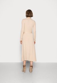 Abito a maglia a coste beige con maniche lunghe, vita aderente e fondo svasato. Abbinato a stivaletti alla caviglia color taupe con cinturini marroni.