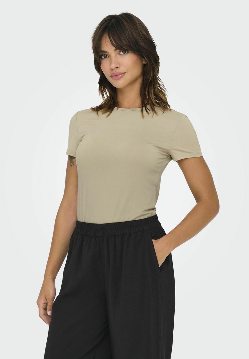 Beige kortærmet t-shirt lavet af glat stof, parret med sorte, elastiske taljebukser med brede ben. Enkel design, ingen synlige mønstre eller accenter.
