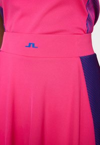 Rosa atletisk klänning med en åtsittande midja och blå logo. Har en asymmetrisk design med vertikala ränder i mörkblått på ena sidan.