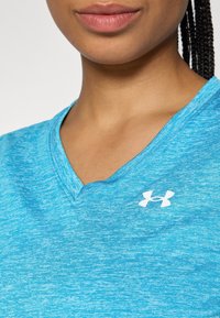 Lähikuva henkilöstä, jolla on päällään sininen Under Armourin V-pääntiainen paita ja sivulla näkyvät punotut hiukset.